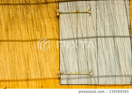 Shadows and light create lines on a yellow wall with a shutter on window in a sunny outdoor setting Shadows and light create lines on a yellow wall with a shutter on window in a sunny outdoor setting 139369365