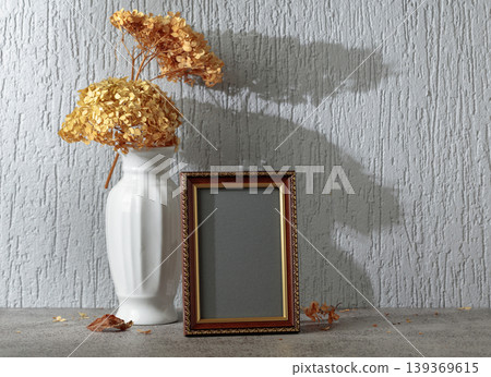 Empty picture frame and white vase with dry flowers on a background of gray wall. Empty picture frame and white vase with dry flowers on a background of gray wall. 139369615