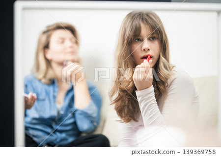 Reflecting girl applying makeup with woman in background Reflecting girl applying makeup with woman in background 139369758