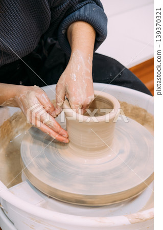 Hands craft clay. Pottery workplace. Unrecognizable experienced woman artisan shaping raw using wheel in professional ceramic studio. 139370321