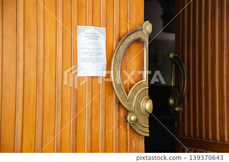 Mosque entrance wooden door with ornate brass handle and posted dua when entering the mosque sign in Arabic and English. Islamic architecture, entrance element, religious practice Mosque entrance wooden door with ornate brass handle and posted dua when entering the mosque sign in Arabic and English. Islamic architecture, entrance element, religious practice 139370643
