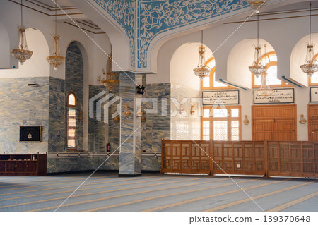 Interior of mosque prayer hall with arches chandeliers columns and mihrab area with carpet rows. Islamic architecture and worship space Interior of mosque prayer hall with arches chandeliers columns and mihrab area with carpet rows. Islamic architecture and worship space 139370648