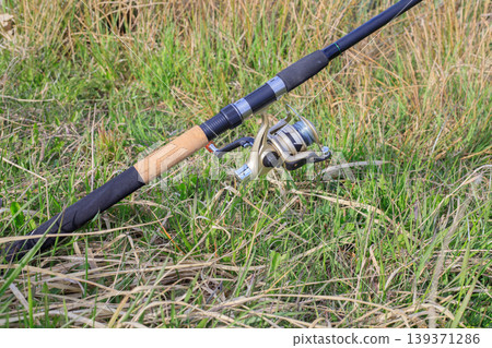 Fishing rod with spinning reel on green grass 139371286