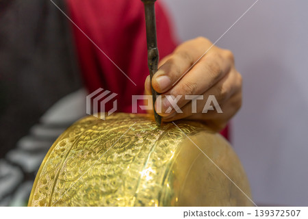 Closeup of artisan engraving intricate patterns on gold surface using tool traditional craftsmanship detail luxury metal work skill 139372507