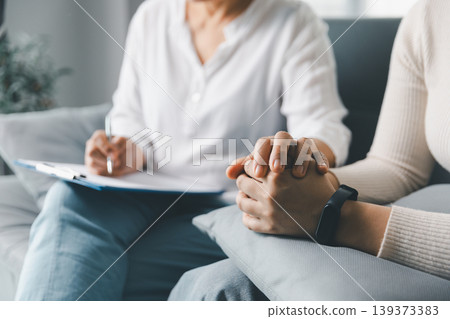 Mental health support concept with therapist touching anxious woman's hands during counseling session at home, showing empathy, trust, reassurance, emotional care, healing and human connection. Mental health support concept with therapist touching anxious woman's hands during counseling session at home, showing empathy, trust, reassurance, emotional care, healing and human connection. 139373383