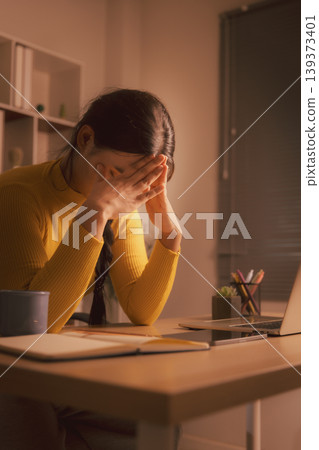 Exhausted young Asian woman covering face while sitting at laptop in cozy home office at night, expressing burnout, anxiety, remote work stress, deadline pressure and mental fatigue. Exhausted young Asian woman covering face while sitting at laptop in cozy home office at night, expressing burnout, anxiety, remote work stress, deadline pressure and mental fatigue. 139373401