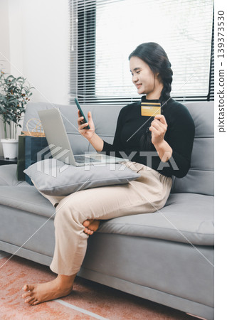 Young Asian woman using smartphone, laptop and credit card for online shopping at home, mobile ecommerce payment, cashless purchase, digital consumer lifestyle and fintech convenience concept Young Asian woman using smartphone, laptop and credit card for online shopping at home, mobile ecommerce payment, cashless purchase, digital consumer lifestyle and fintech convenience concept 139373530