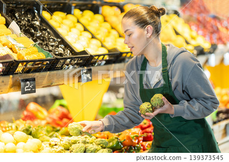 Young woman seller puts artichokes in vegetable shop 139373545