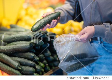 Close-up of female seller's hands putting cucumbers into plastic bag Close-up of female seller's hands putting cucumbers into plastic bag 139373568