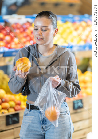 Young woman chooses oranges in store Young woman chooses oranges in store 139373573
