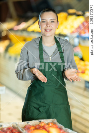 woman seller standing on the background of vegetables and fruits in supermarket woman seller standing on the background of vegetables and fruits in supermarket 139373575