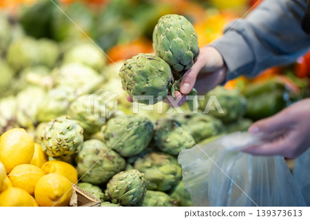 Shopper selects ripe artichokes at grocery supermarket closeup Shopper selects ripe artichokes at grocery supermarket closeup 139373613