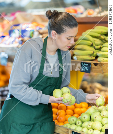 Young female seller putting pears in vegetable shop Young female seller putting pears in vegetable shop 139373665
