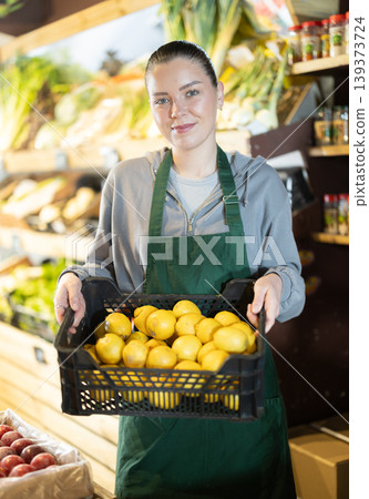 Young female shop assistant with crate of lemons in store Young female shop assistant with crate of lemons in store 139373724