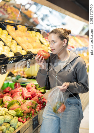 woman stands near the counter in a supermarket and chooses a farm bell pepper woman stands near the counter in a supermarket and chooses a farm bell pepper 139373740
