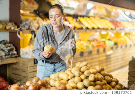 woman stands near the counter in the vegetable section and chooses potatoes woman stands near the counter in the vegetable section and chooses potatoes 139373765
