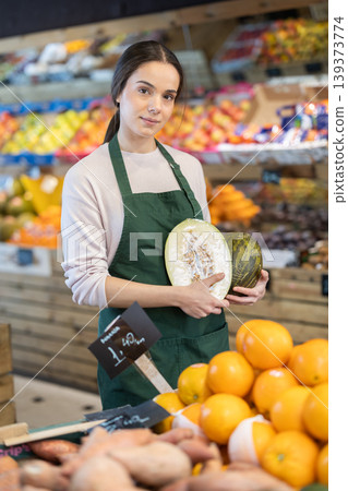 Young woman seller puts melon in store Young woman seller puts melon in store 139373774
