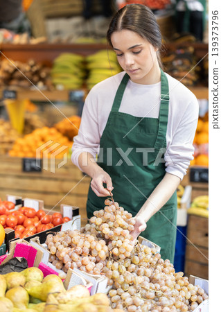 Female seller places ripe grape on display case Female seller places ripe grape on display case 139373796