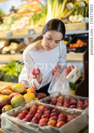 Young woman chooses plums in store Young woman chooses plums in store 139373803