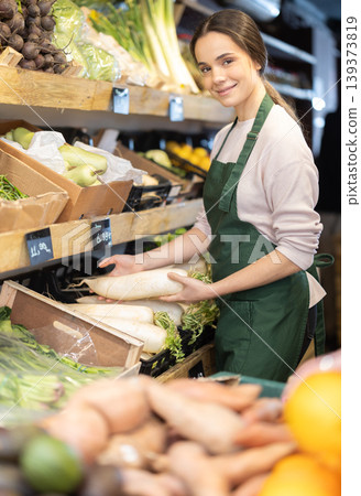 Young woman seller puts daikon in vegetable shop Young woman seller puts daikon in vegetable shop 139373819
