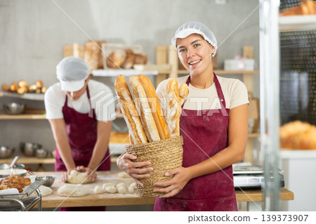 Young female baker holding baguettes in round wicker basket Young female baker holding baguettes in round wicker basket 139373907