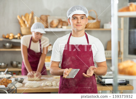 Young baker guy is standing near work table in kitchen, working with dough Young baker guy is standing near work table in kitchen, working with dough 139373932