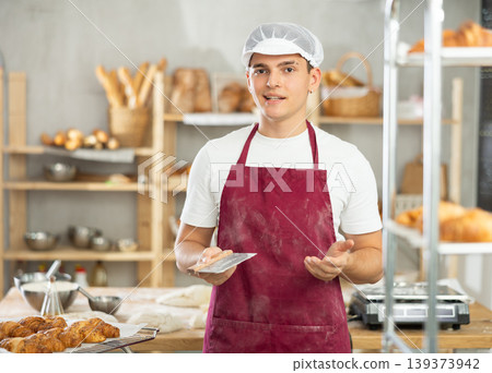 Portrait of young male baker holding knife cutting raw dough in bakery kitchen Portrait of young male baker holding knife cutting raw dough in bakery kitchen 139373942