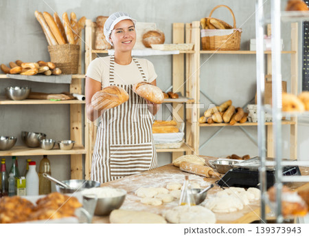 Enthusiastic young female baker presenting golden freshly baked bread Enthusiastic young female baker presenting golden freshly baked bread 139373943