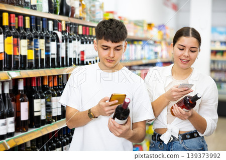 Young couple scanning barcodes on bottles of alcoholic beverages with smartphones Young couple scanning barcodes on bottles of alcoholic beverages with smartphones 139373992