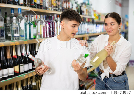Couple reading labels on bottles of alcoholic drinks in supermarket 139373997