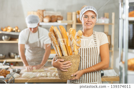 Young female baker holding baguettes in round wicker basket Young female baker holding baguettes in round wicker basket 139374011