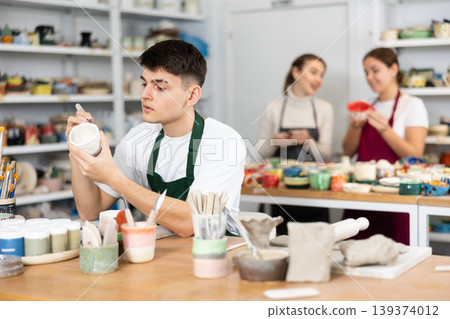 Young man painting pottery in workshop Young man painting pottery in workshop 139374012