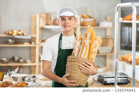 Young male baker holding baguettes in round wicker basket 139374041