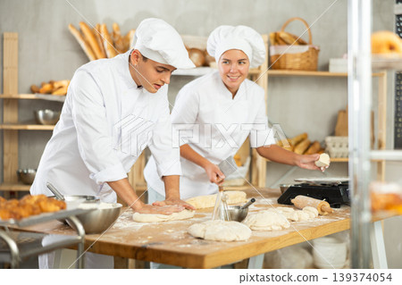 Friendly young bakers kneading and portioning dough in artisan bakery Friendly young bakers kneading and portioning dough in artisan bakery 139374054