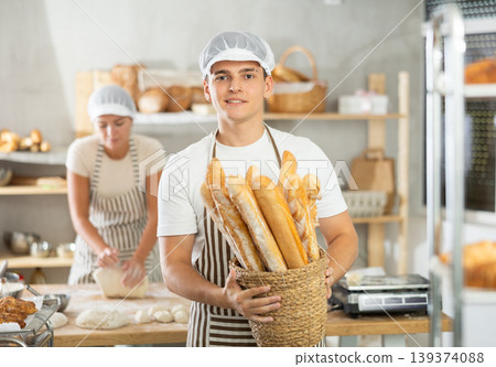 Happy male baker posing with basket of freshly baked baguettes in bakery, demonstrating concept of food industry and baker profession 139374088