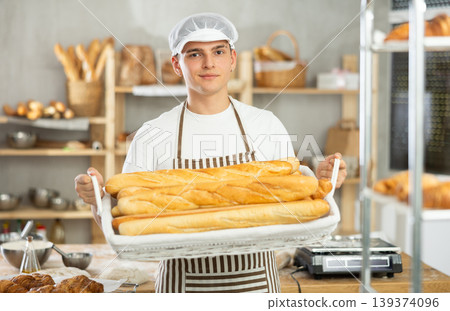 Young male baker holding baguettes in wicker basket 139374096