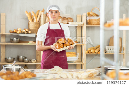 Young male baker holding croissants in square wicker basket Young male baker holding croissants in square wicker basket 139374127