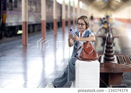 Asian adult woman tourist traveler mobile phone use waiting train platform railway station passenger journey public transportation connection 139374374