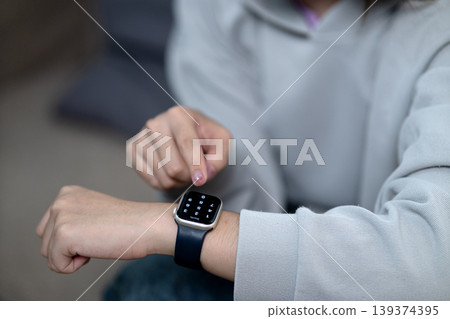 Asian young adult person finger touching smartwatch screen inputting pin code secure smart wearable technology device access control indoors home Asian young adult person finger touching smartwatch screen inputting pin code secure smart wearable technology device access control indoors home 139374395