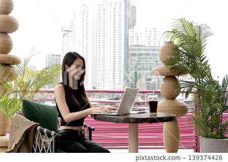Asian woman laptop remote work city cafe outdoor setting modern urban lifestyle digital nomad professional 139374426