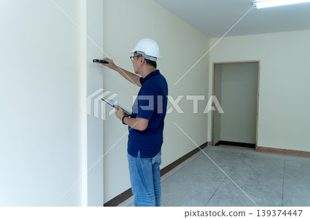 Adult Asian Construction Engineer Inspecting Wall Alignment Using Level Tool Documenting Quality Control New Building Project Site 139374447