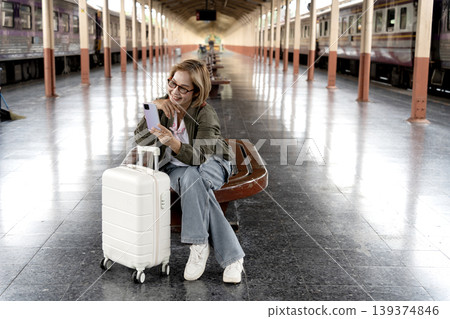 Adult Asian traveler woman using smartphone communication at busy train station platform smiling happy while waiting for journey Adult Asian traveler woman using smartphone communication at busy train station platform smiling happy while waiting for journey 139374846