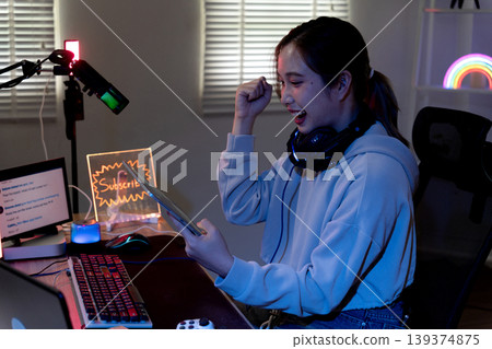 Asian young adult woman gamer streamer celebrating victory playing online video game livestreaming at home gaming setup night room Asian young adult woman gamer streamer celebrating victory playing online video game livestreaming at home gaming setup night room 139374875