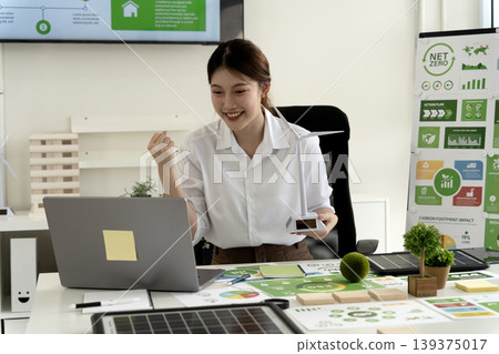 Asian adult woman celebrates renewable energy project success working on net zero carbon reduction green business strategy in office environment sustainability meeting 139375017