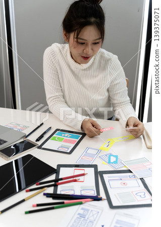 Asian young adult woman user experience designer creates mobile app wireframes prototyping digital interface layouts office workspace Asian young adult woman user experience designer creates mobile app wireframes prototyping digital interface layouts office workspace 139375071