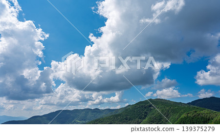 Many white clouds drift across the bright blue summer sky, and the mountains are covered in green. 139375279