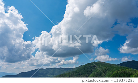 Many white clouds drift across the bright blue summer sky, and the mountains are covered in green. Many white clouds drift across the bright blue summer sky, and the mountains are covered in green. 139375283