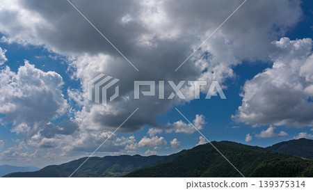 Many white clouds drift across the bright blue summer sky, and the mountains are covered in green. 139375314