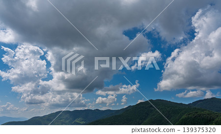 Many white clouds drift across the bright blue summer sky, and the mountains are covered in green. Many white clouds drift across the bright blue summer sky, and the mountains are covered in green. 139375320