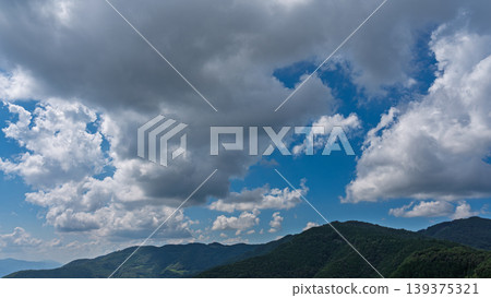 Many white clouds drift across the bright blue summer sky, and the mountains are covered in green. Many white clouds drift across the bright blue summer sky, and the mountains are covered in green. 139375321